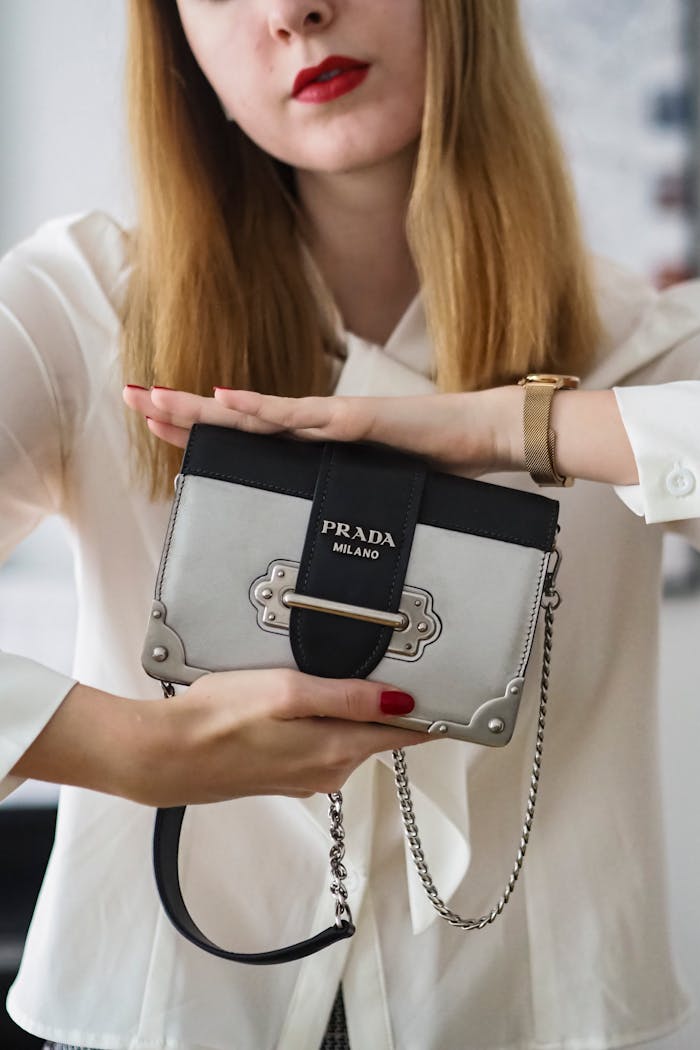 Close-up of a woman showcasing a gray and black Prada Milano handbag indoors.